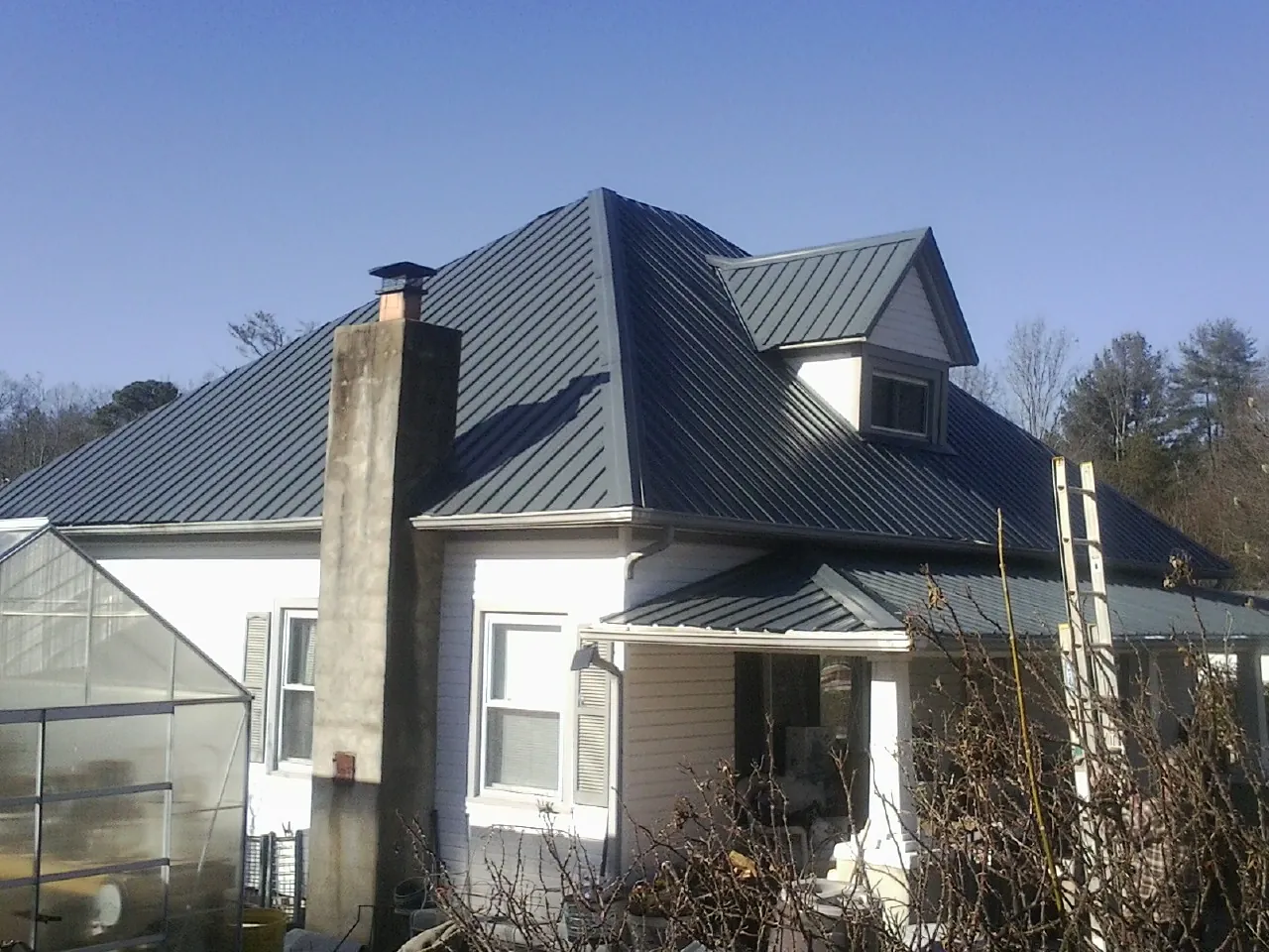 Dark blue standing seam metal roof on a white farmhouse with dormer — Slate & Tile Roof Repair by Roofing Brothers in Crystal Spring