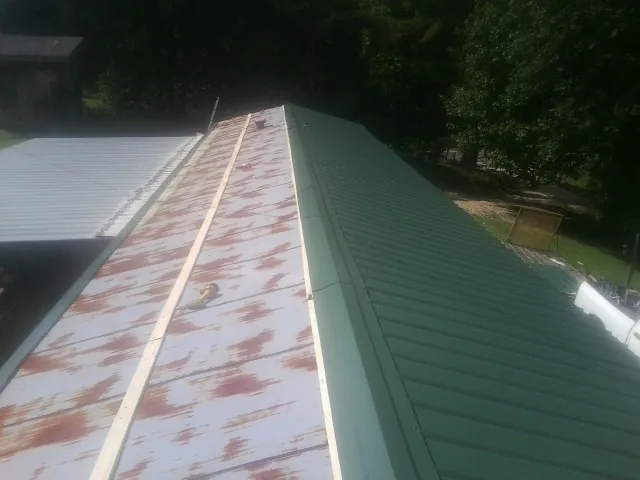 Old rusted panels beside newly installed green metal roofing — Wind Damage Roof Repair by Roofing Brothers in Crystal Spring