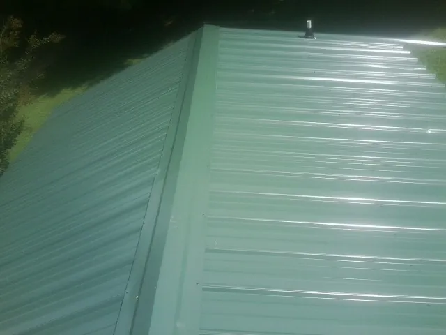 New green metal panels meeting at the ridge of a roof — Flat Roof Repair work by our crew in Crystal Spring