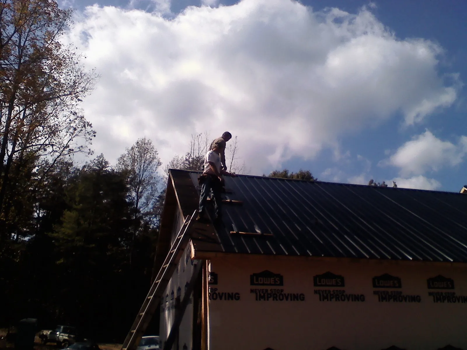 Roofer fastening dark metal panels high against a cloudy sky, from a Roof Inspection job in Crystal Spring